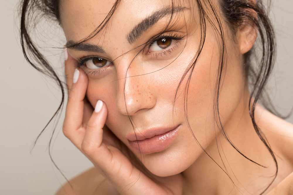 Close-up of a woman's face with one hand on her cheek against a neutral background