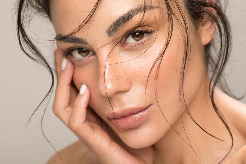 Close-up of a woman's face with one hand on her cheek against a neutral background